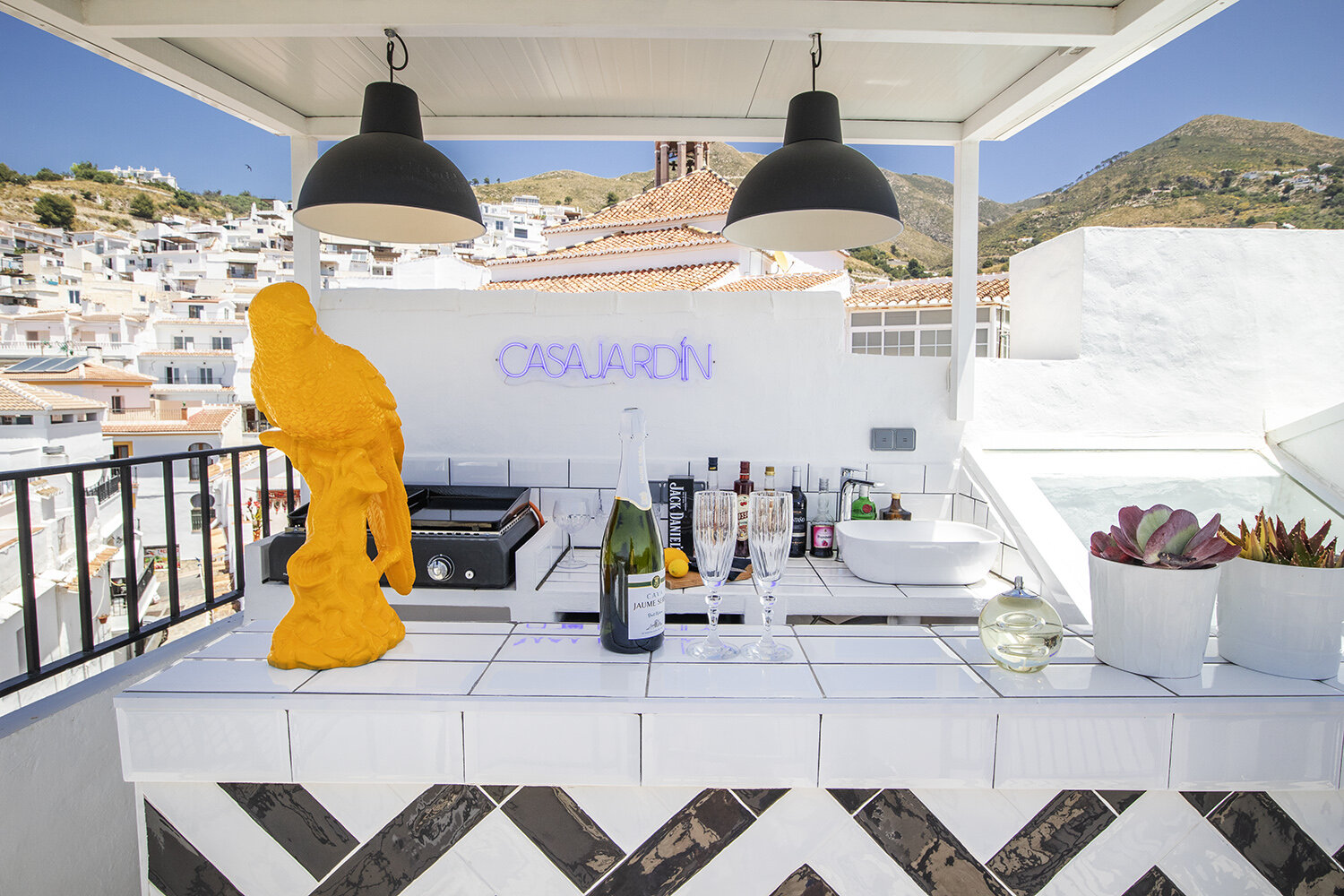 The rooftop honesty bar at Casa Jardín — chilled cava, the Casa Jardín neon sign, and the white-washed roofs of Cómpeta beyond.