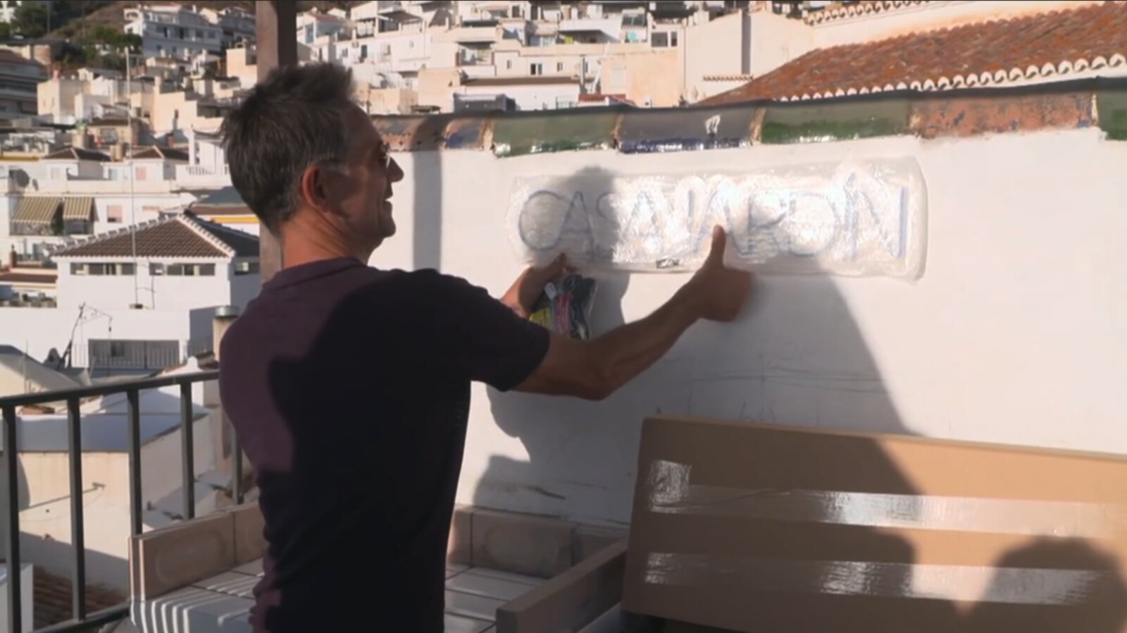 Anthony placing the Casa Jardín name on the rooftop, the white-washed houses of Cómpeta visible behind.